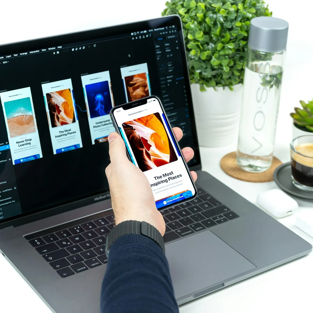 A hand is holding a smartphone above paper app design sketches, seen from above.
